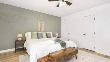 Une chambre à coucher comprenant un lit, des tables de chevet, un banc, un ventilateur de plafond et une armoire.