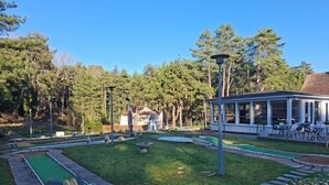 A miniature golf course with a green putting area, a small pond, and a covered seating area with outdoor tables and chairs. - Logis La Dunette Quend 3* House with Garden & Spa (Quend)