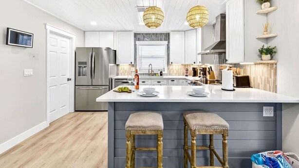 Een moderne keuken met een centraal eiland, roestvrijstalen apparatuur en houten barkrukken.