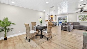 Een moderne woonkamer met een eethoek, met een ronde tafel met stoelen, een bank en een plafondventilator.