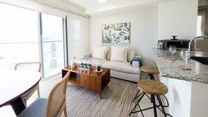 A modern living room with a sofa, coffee table, and dining area. There is a kitchen with a sink and a clock. - Ventanas Ocean View -V3-8A- 2 bed, 2 bath (Punta Chame)