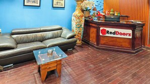 A reception area with a leather sofa, a glass-top coffee table, a wooden reception desk with 'RedDoorz' signage, and a blue wall with framed pictures. - Xumi Motel (Hanoi)