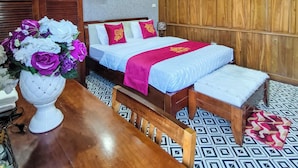 A hotel room with a wooden ceiling, a bed with a red and white bedspread, a wooden bench, a table with a vase of flowers, and a patterned floor. - Xumi Motel (Hanoi)