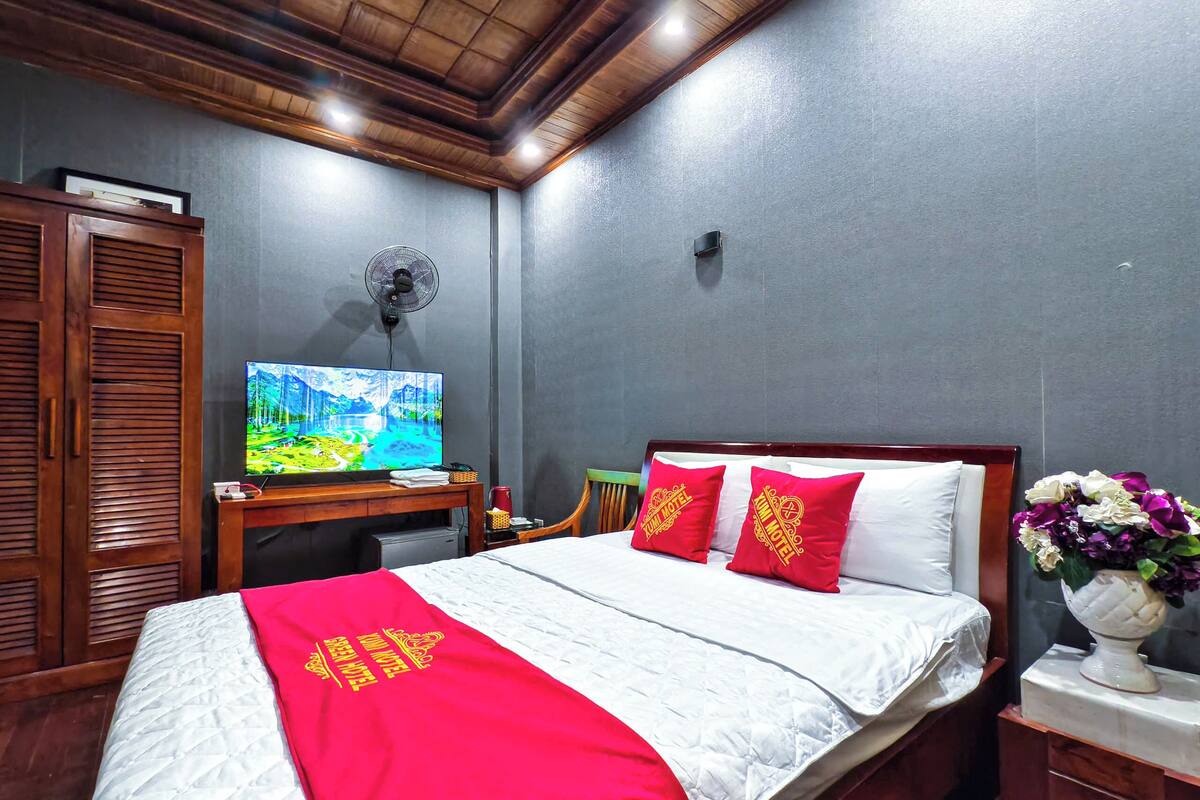 Ein Hotelzimmer mit Bett, Fernseher, Schreibtisch und Ventilator.