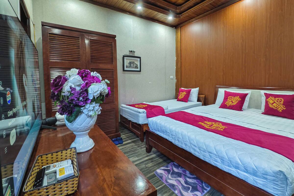 Ein Hotelzimmer mit zwei Betten, Holzkopfteilen, einer Holzbalkendecke, einem gerahmten Bild an der Wand und einer Vase mit Blumen auf einem Tisch.