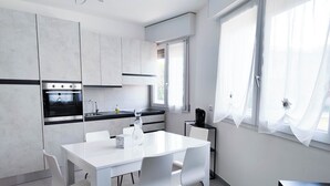 Ett modernt kök med vita skåp, en inbyggd ugn, en kaffemaskin och en matplats med ett vitt bord och stolar.