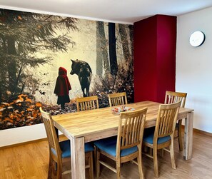 A dining area with a wooden table and chairs, a red accent wall, and a mural depicting a person and a wolf in a forest. - FEWO Unterm Stein - Entire House - 5 Bedrooms (Alheim)