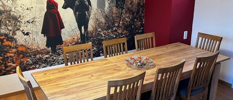 A dining area with a wooden table and chairs, a red accent wall, and a mural of a forest scene.