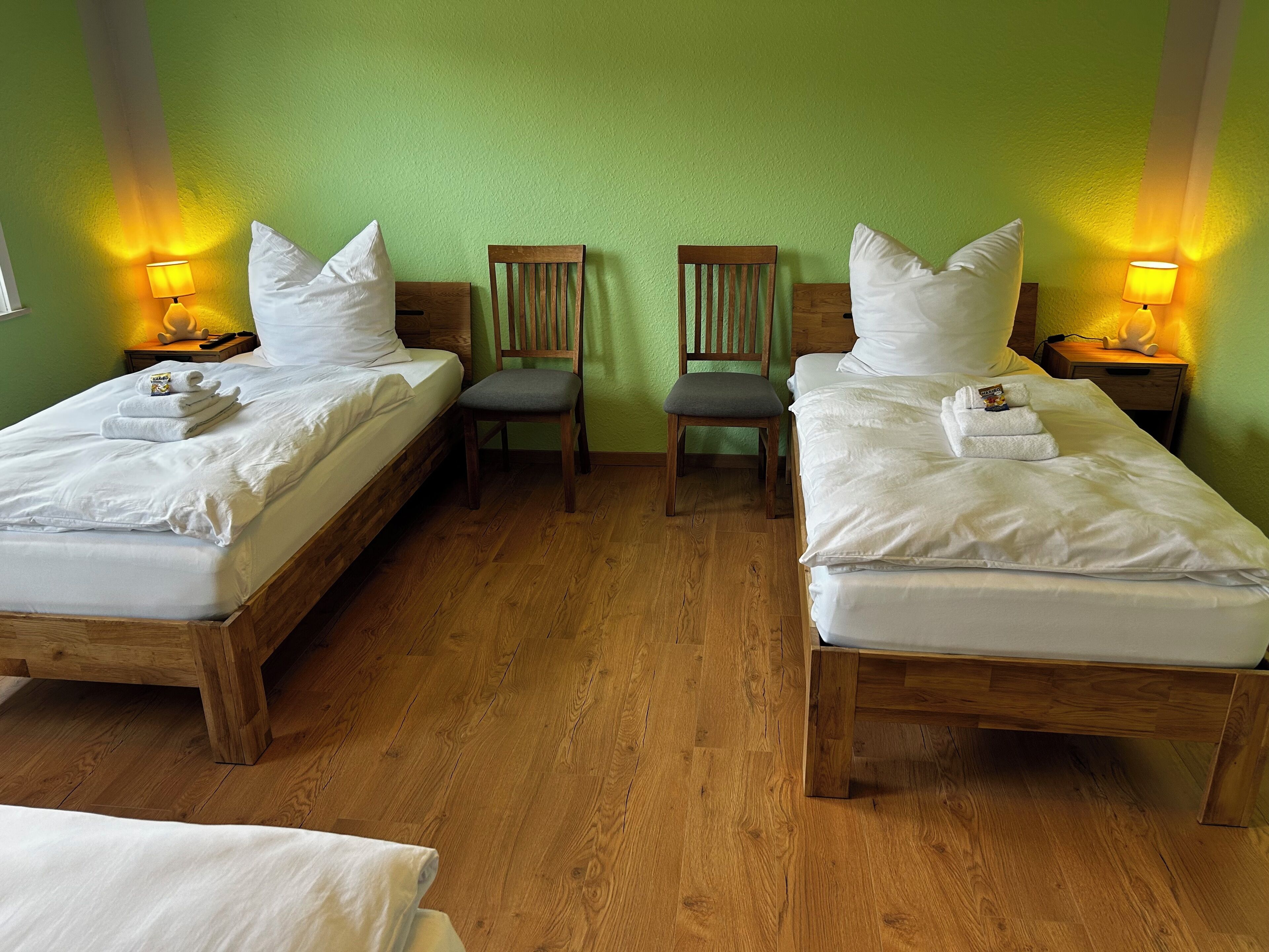 A room with two wooden beds, each with white bedding and pillows, and a chair between them.