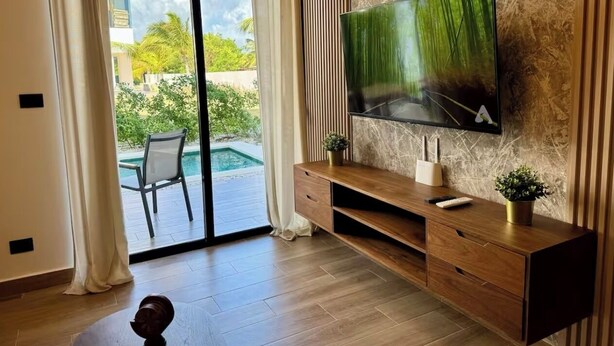 Ein modernes Wohnzimmer mit einem großen Flachbildfernseher an einer Marmorwand, einer Holz-Unterhaltungseinrichtung und einer Glasschiebetür, die zu einem Poolbereich führt.