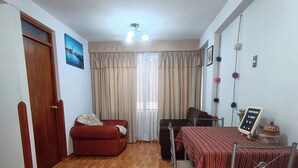 A spacious living room with a wooden floor, a red sofa, a dining table with chairs, and a large window with curtains. - Eli's home (Cusco)