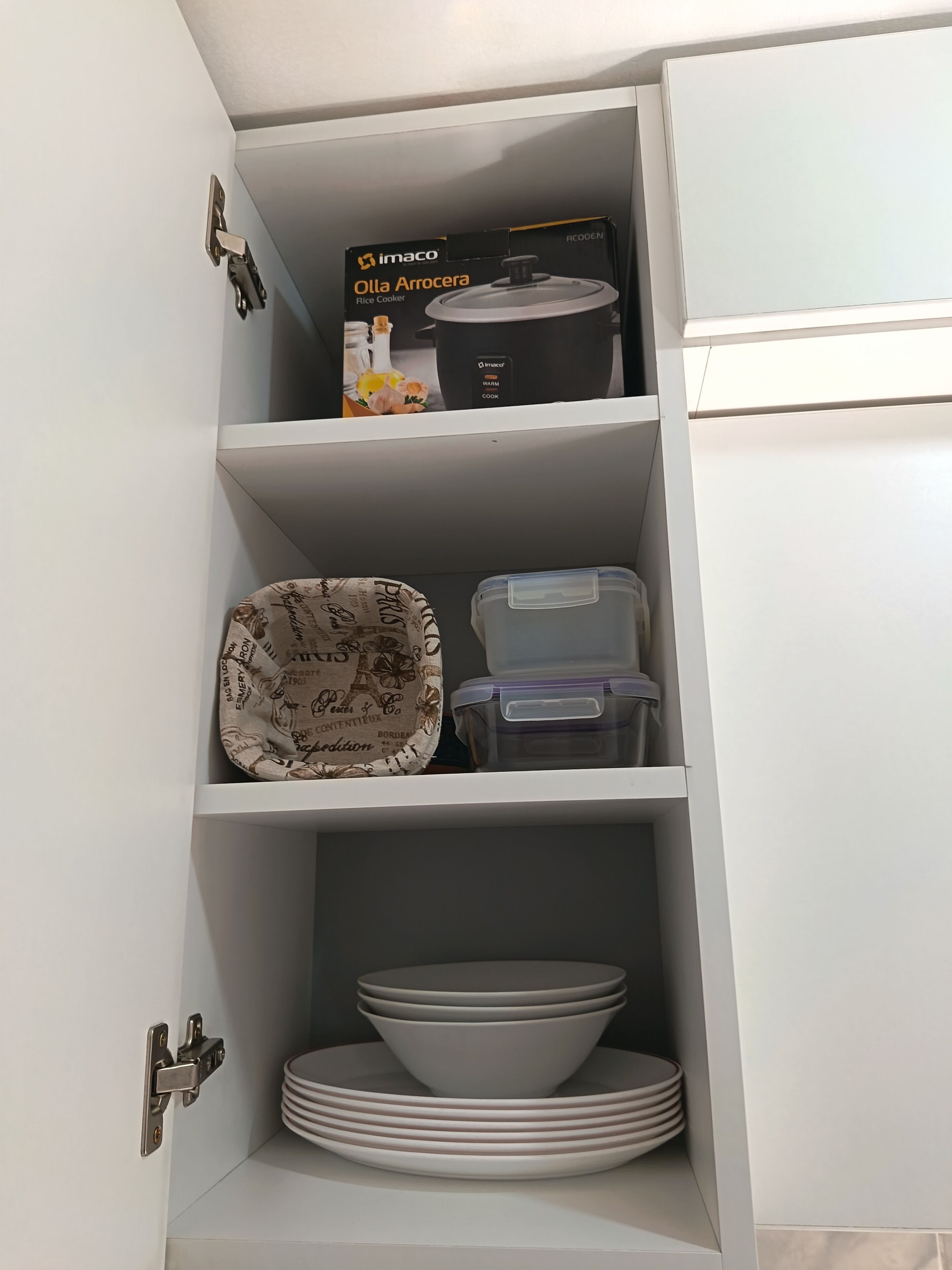 A kitchen cabinet with a rice cooker, a patterned plate, and stacked plates.