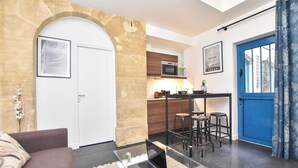 A compact living space with a kitchenette, a dining area with stools, a sofa, and a glass coffee table. - Superb Apartment-1br/3p - Sentier (Paris)