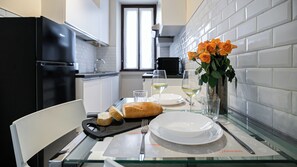 A dining table set with plates, glasses, a loaf of bread, a vase with flowers, and a fork. - Italianway Easy - Leoncavallo 45 (Milan)