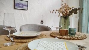 Une table à manger avec des assiettes, des couverts et des verres, un vase rempli de fleurs et un tableau encadré accroché au mur.