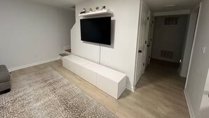 Ein modernes Wohnzimmer mit einem Flachbildfernseher, der an einer weißen Unterhaltungsanlage befestigt ist, einem grauen Sofa und einem gemusterten Teppich.