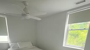Ein Schlafzimmer mit einem Bett, einem Deckenventilator, einem Fenster und einem Mülleimer.