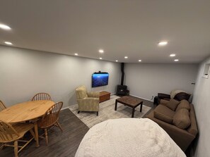 A cozy living room with a wooden dining table, a sofa, a TV mounted on the wall, and a fireplace. - 5-bedrooms, Tons of Outdoor Space, Central Location! (Kalispell)