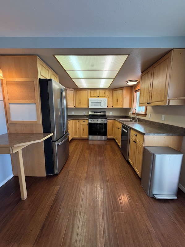 A kitchen with wooden cabinets, a stainless steel refrigerator, a microwave, a stove, and a dishwasher. - 5-bedrooms, Tons of Outdoor Space, Central Location! (Kalispell)