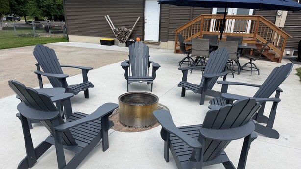 Un patio con sillas Adirondack dispuestas alrededor de un brasero, una terraza de madera y una puerta de garaje al fondo.