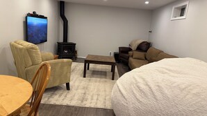 Una habitación acogedora con sofá, sillón y una pequeña mesa. Hay una chimenea y un televisor montado en la pared.