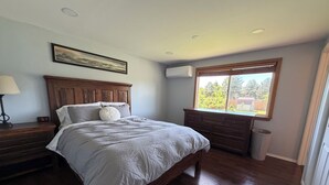 Un dormitorio con una cama de madera, una mesita de noche, un aparador, un ventanal con vistas y un equipo de aire acondicionado.