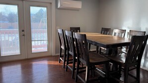 Comedor con mesa y sillas de madera, un equipo de aire acondicionado y vistas a través de un ventanal.