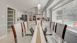 A modern kitchen with white cabinets, a dining area with a glass table, and a view of a backyard with a pool. - Paradise Garden Resort And Spa (Houston)