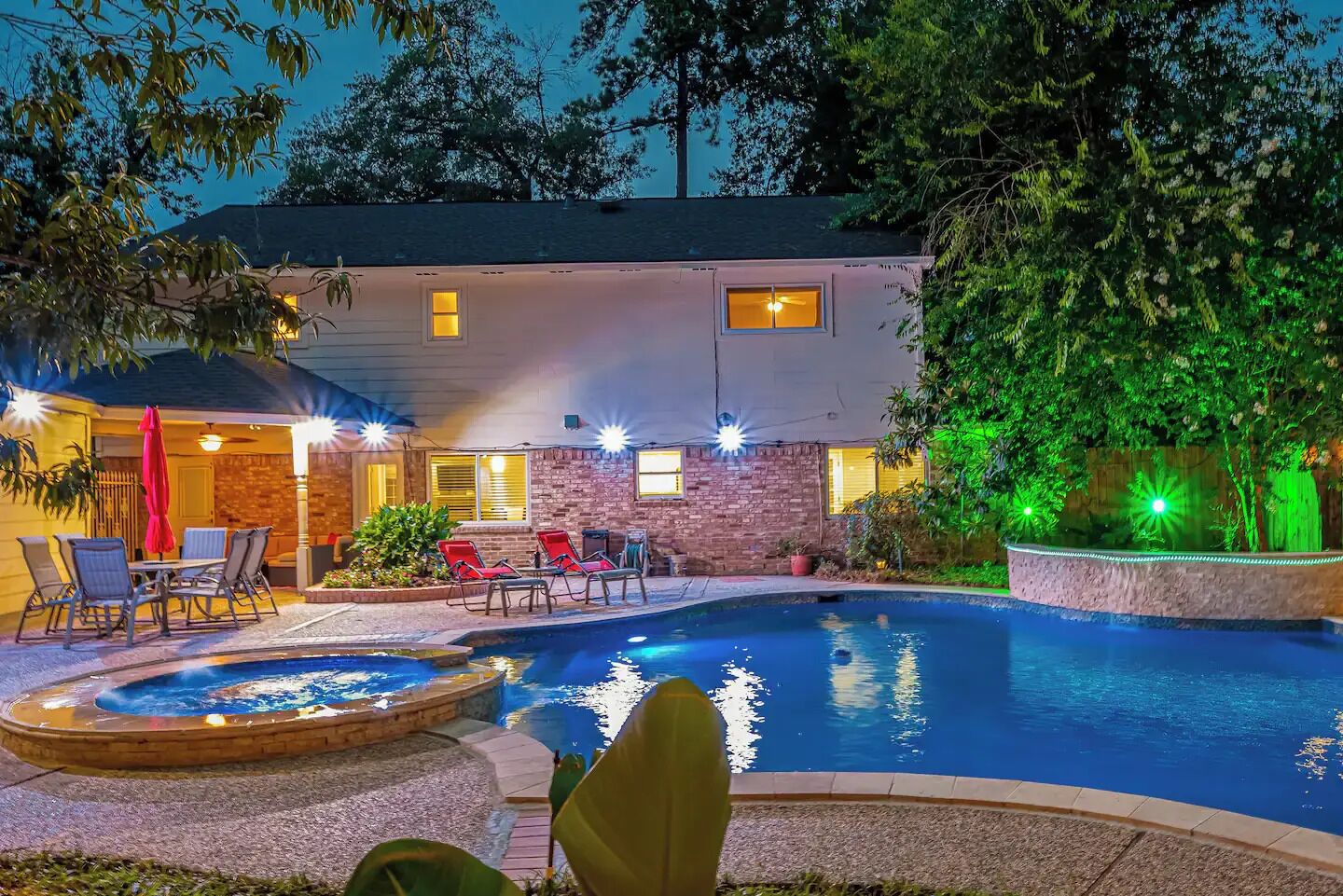 A pool area with a hot tub, lounge chairs, and a brick building with windows.