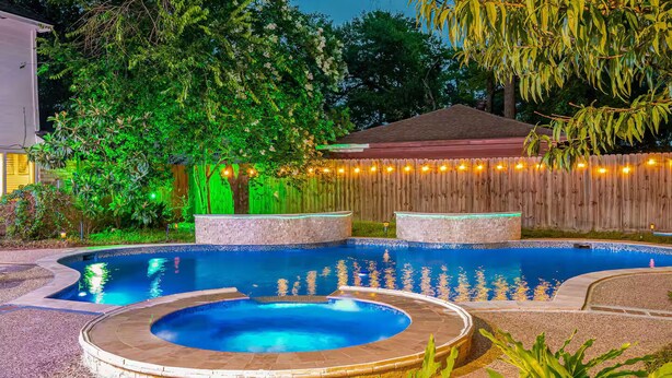 A swimming pool with a hot tub, surrounded by a wooden fence and trees. - Paradise Garden Resort And Spa (Houston)
