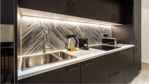 A modern kitchen with a marble backsplash, stainless steel sink, and black cabinets. - HOTEL BOETIE - CHAMPS ELYSEES  (Paris)