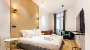 A modern hotel room with a large bed, a desk with a flat-screen TV, a seating area with a sofa, and a balcony with a view. - HOTEL BOETIE - CHAMPS ELYSEES  (Paris)