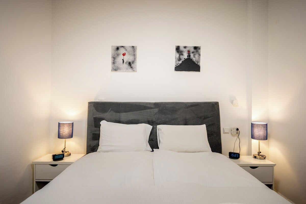 A neatly made bed with white linens, two bedside tables with lamps, and two wall-mounted artworks.