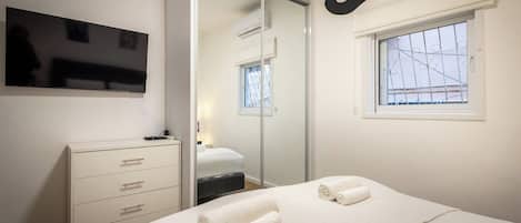 A bedroom with a bed, a dresser, a television, a window, and a mirror.