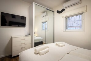 Een slaapkamer met een bed, een dressoir, een televisie, een raam en een spiegel.