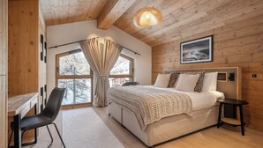 Ein Schlafzimmer mit Holzboden, einem großen Bett mit weißem Kopfteil, einem Schreibtisch mit Stuhl und einem Fenster mit Vorhängen.