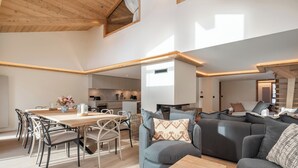 Ein geräumiger Wohnbereich mit Holzboden, einem Esstisch mit Stühlen und einem grauen Sofa mit gemusterten Kissen.