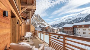 Ein hölzerner Balkon mit Blick auf schneebedeckte Berge und ein Holzhaus im Hintergrund.