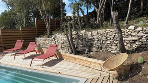 En træterrasse med en pool, røde liggestole og en stenvæg.