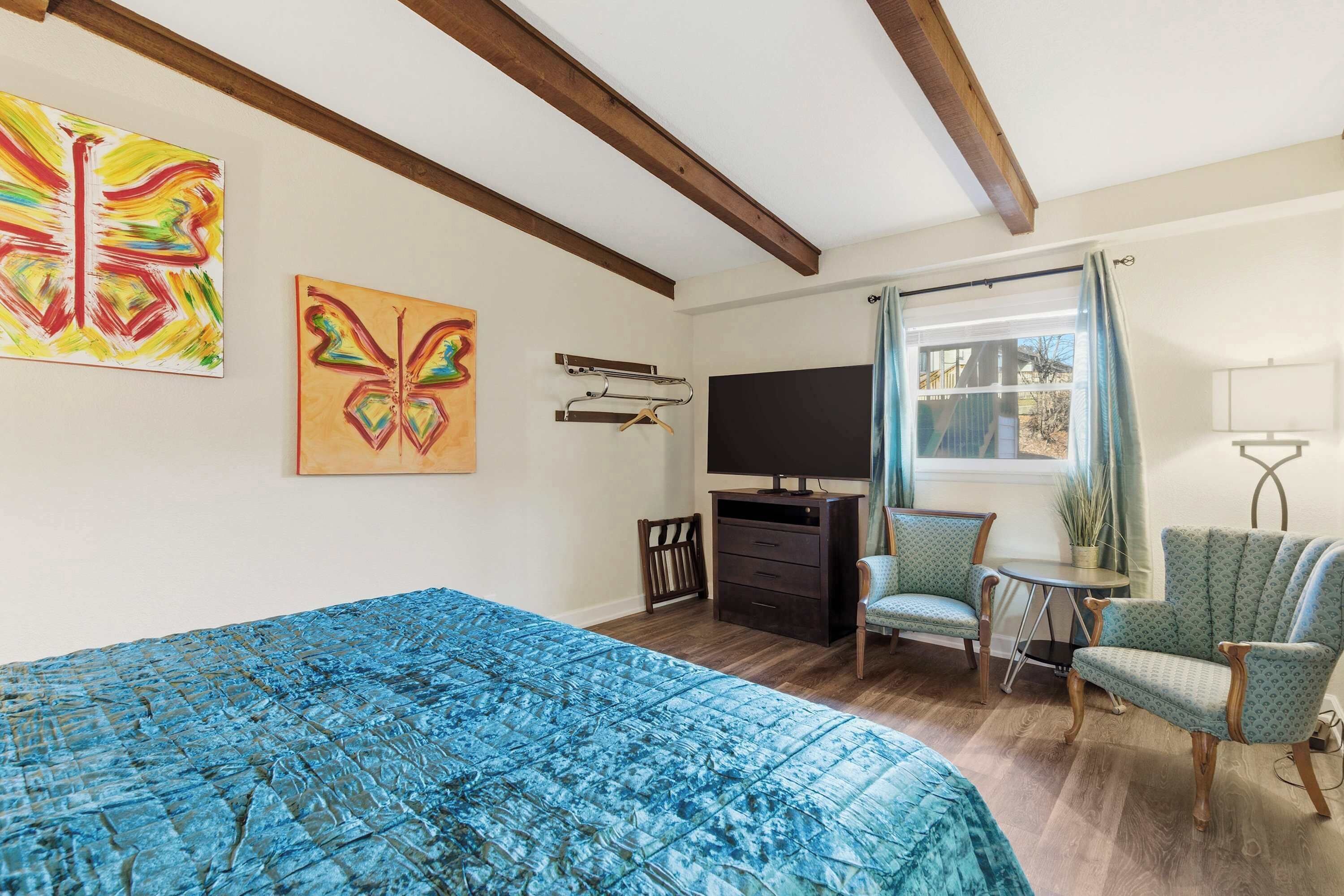 A bedroom with a bed, two chairs, a TV, and artwork on the wall.