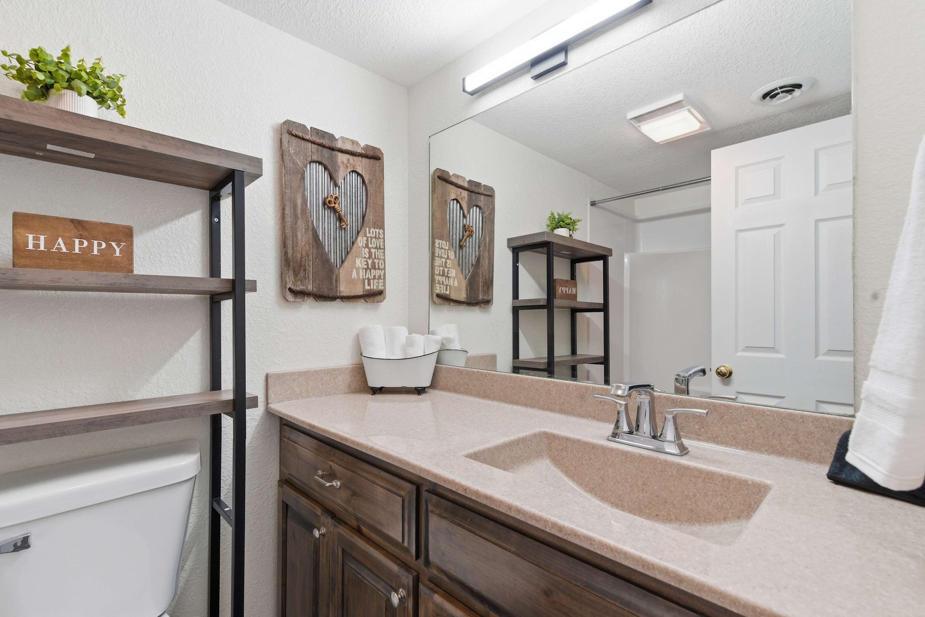 A bathroom with a beige countertop, a white sink, a mirror, and wooden shelves with decorative items.