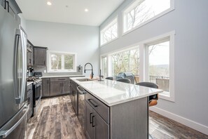 A modern kitchen with a large island, stainless steel appliances, and large windows. - New! Modern Lake Access Home w/ Hot Tub! (Swanton)