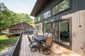 A deck with a table and chairs, overlooking a backyard with a wooden deck and a house. - New! Modern Lake Access Home w/ Hot Tub! (Swanton)