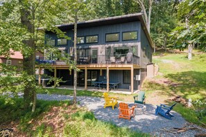A two-story building with a balcony and outdoor seating area. - New! Modern Lake Access Home w/ Hot Tub! (Swanton)