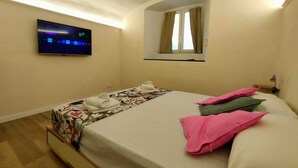 Ein Hotelzimmer mit Bett, Wand-Fernseher, Fenster mit Vorhängen und einem kleinen Tisch mit Handtüchern.