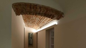 Ein schmaler Gang mit Holzboden, einem Backsteinbogen und einer weißen Tür am Ende.