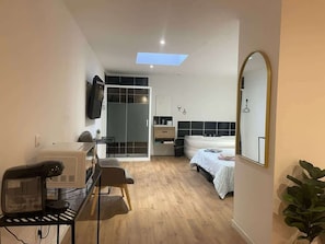 A modern hotel room with a bed, a desk, a chair, a TV, and a large mirror. - Le Nid Cosy avec Balnéo (Tourcoing)