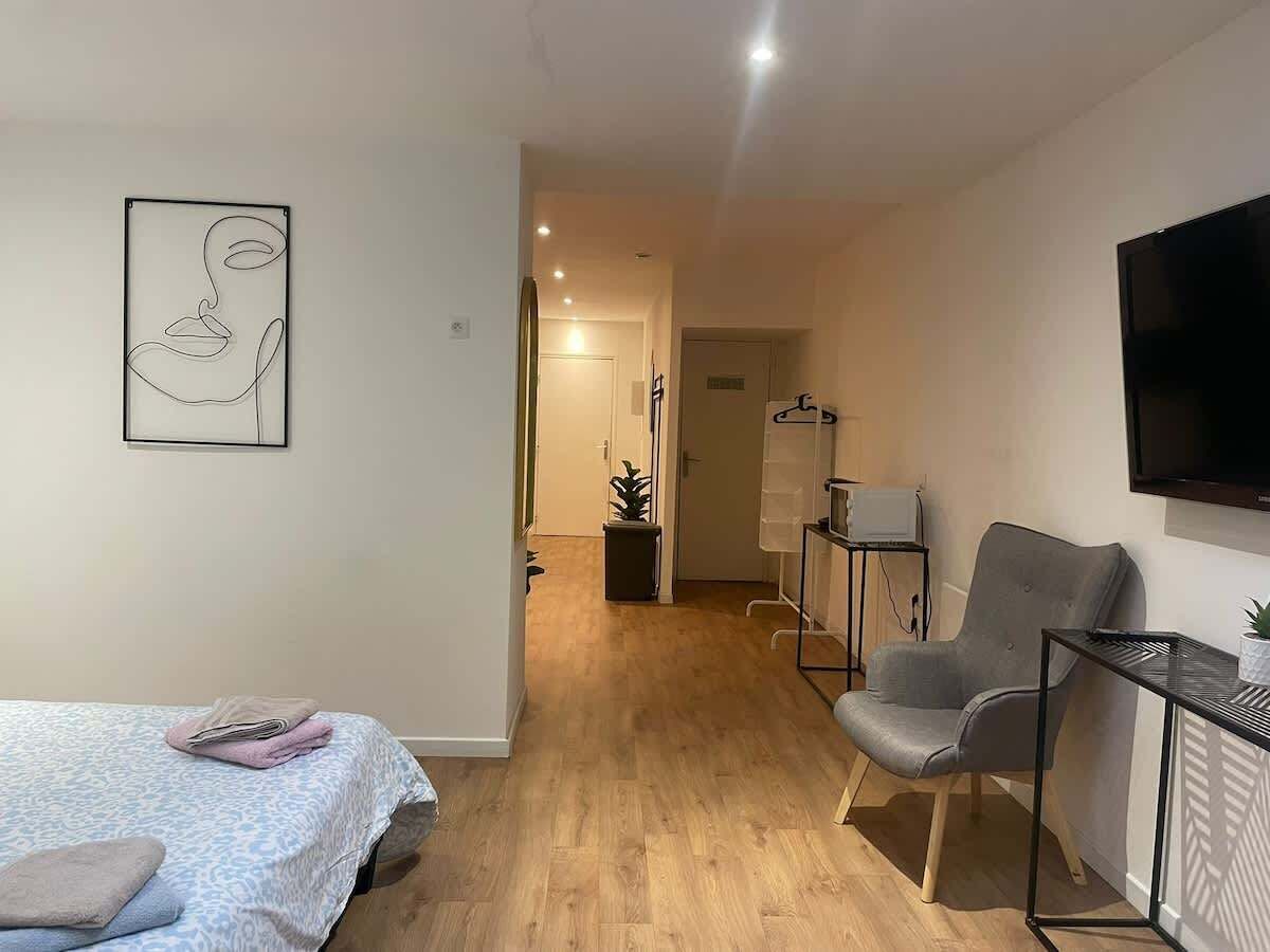 A modern room with a bed, a grey armchair, a TV, and a small table.