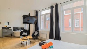 Quarto de hotel moderno com cama, televisão, área de estar com cadeiras e vista para o exterior.