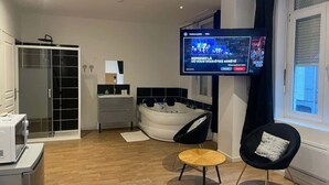 Uma sala de estar moderna com televisão de tela plana, uma poltrona preta, uma mesa de madeira redonda, uma banheira branca e um armário com portas de vidro.